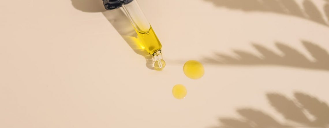 A dropper with jojoba oil drops on a cream background