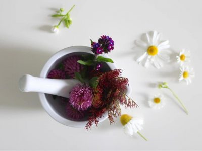 A mortar and pestle with natural flowers sprinkled around on a white desk